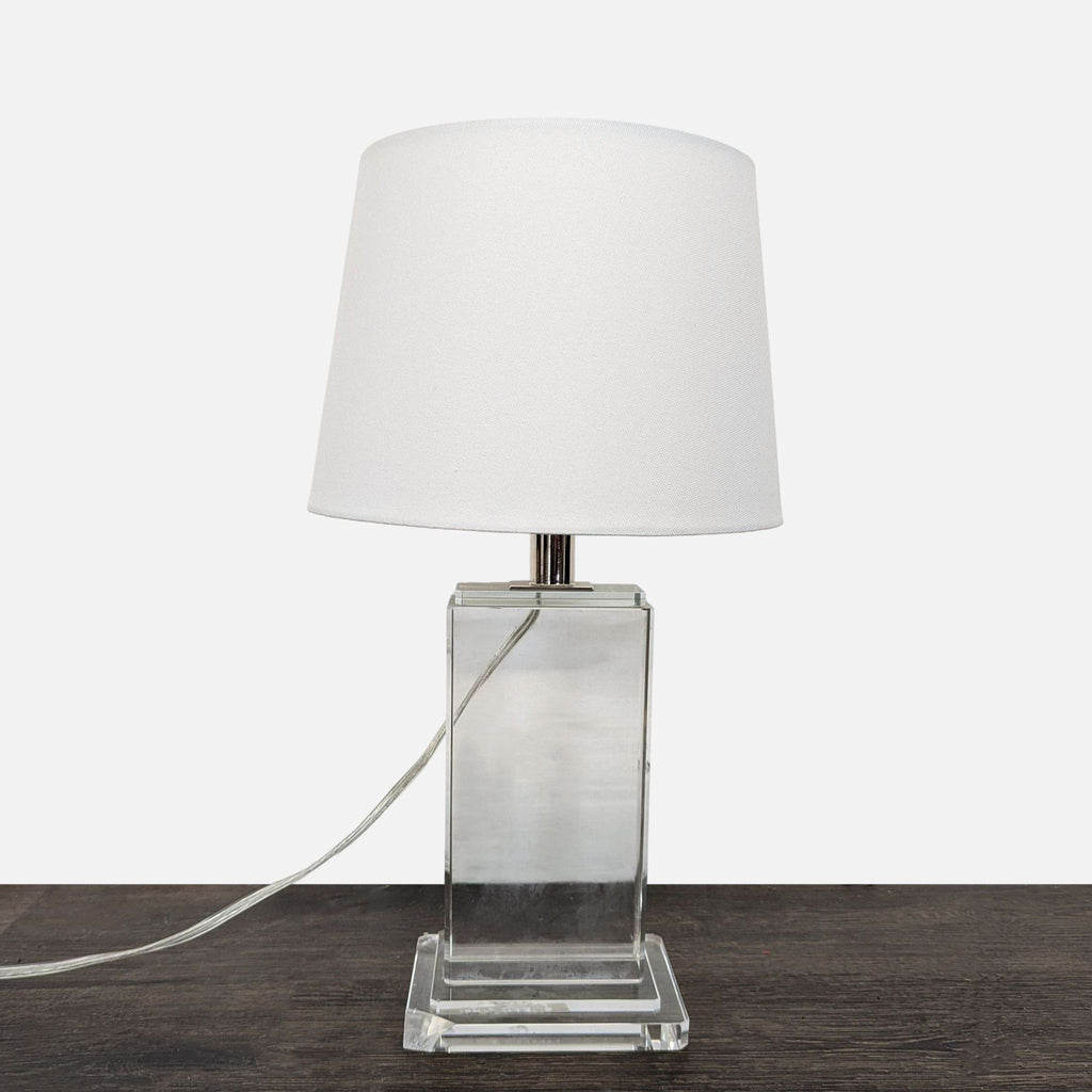 Modern table lamp with clear base and white shade, suitable for desks or nightstands.