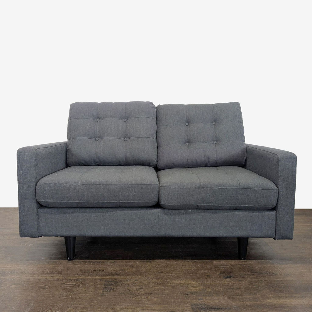 Dark gray loveseat with tufted cushions, wooden legs, and compact design for small living spaces.