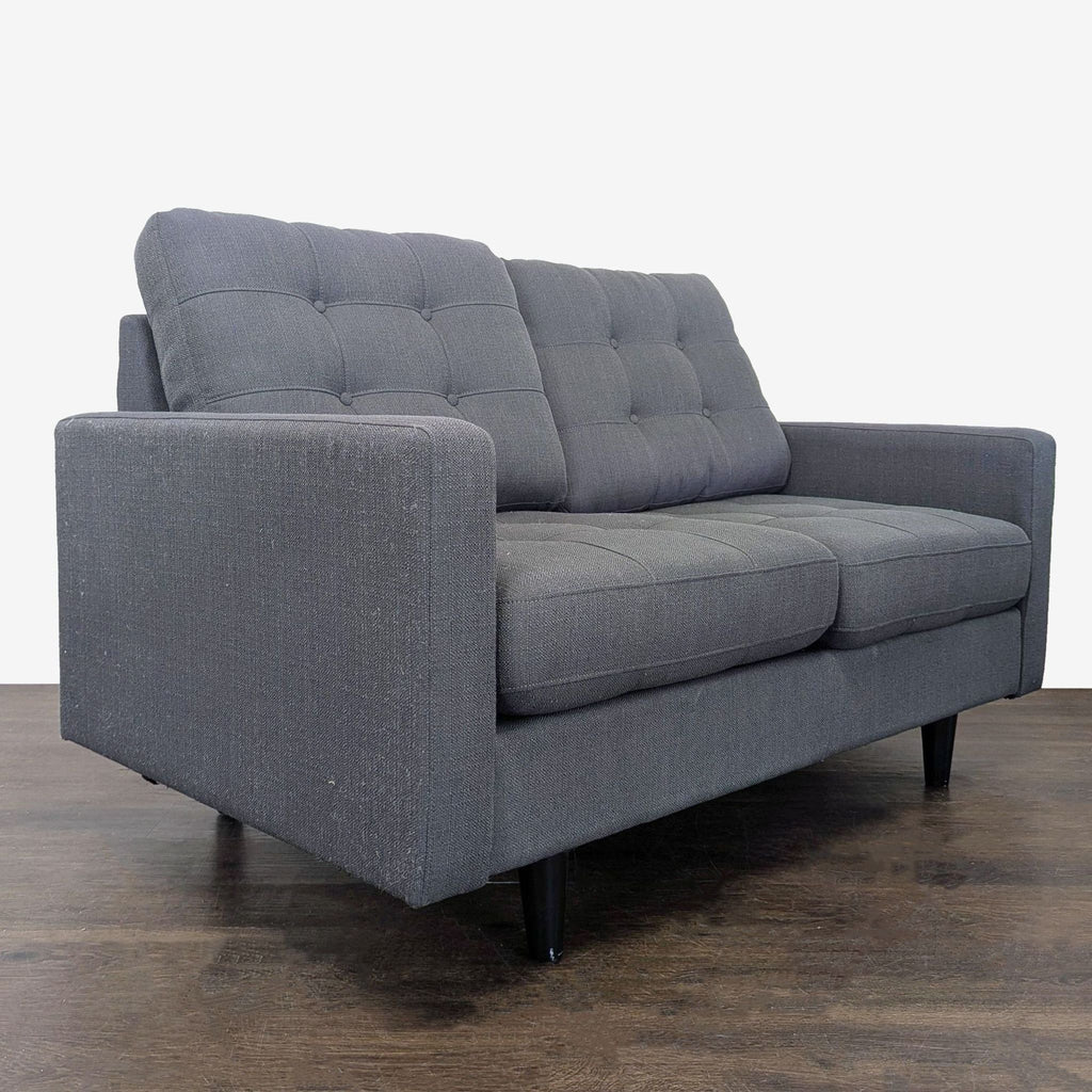 Compact loveseat upholstered in soft dark gray fabric, featuring comfortable tufted cushions and sturdy wooden legs.