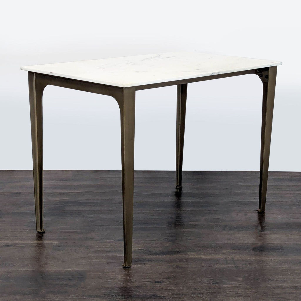 CB2 French kitchen-inspired dining table featuring polished marble slab atop sculptural brass-finished metal base.