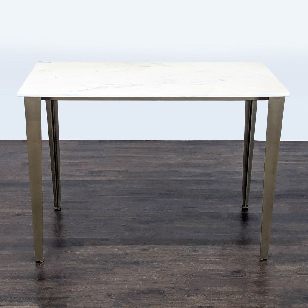 CB2 industrial-style table with white Carrara marble top and antiqued brass-finished sculptural legs, seats six.