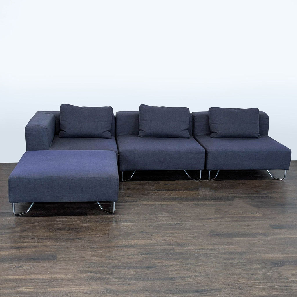 Sleek CB2 sofa features dark blue upholstery, chrome metal legs, spacious seating, and a lounge chaise.