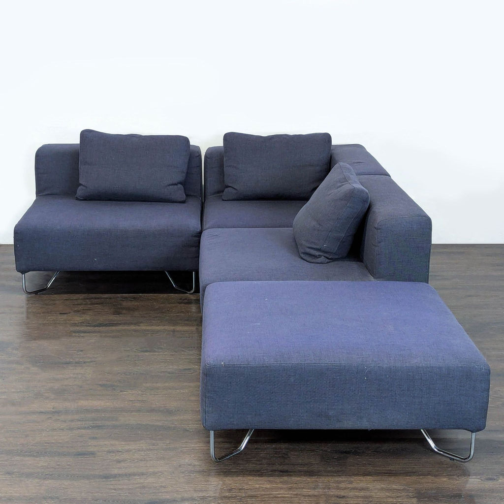 Modern CB2 dark blue sectional with three seats, chaise section, chrome legs, and plush matching back cushions.