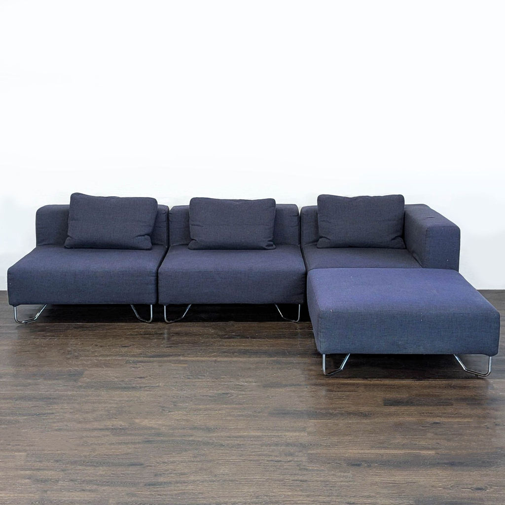CB2 sectional sofa in dark blue fabric with chrome legs, chaise lounge, and matching cushions for comfort.