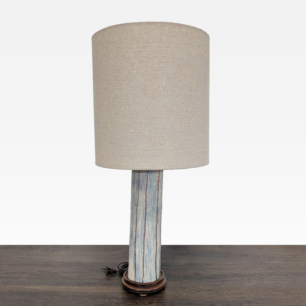 Modern table lamp with beige fabric shade and pottery base with blue and brown stripes, for cozy lighting.