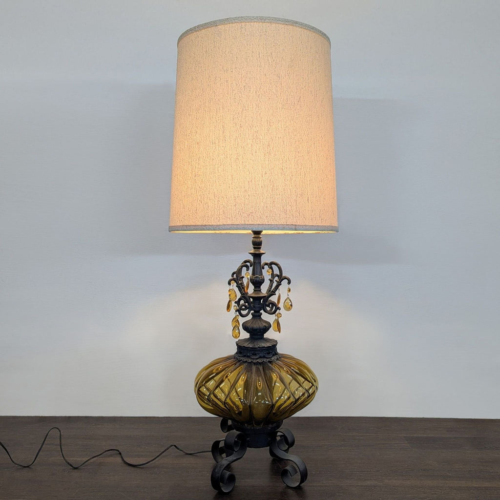 Amber glass and metal table lamp with tall fabric shade and decorative hanging accents, evoking a classic style.