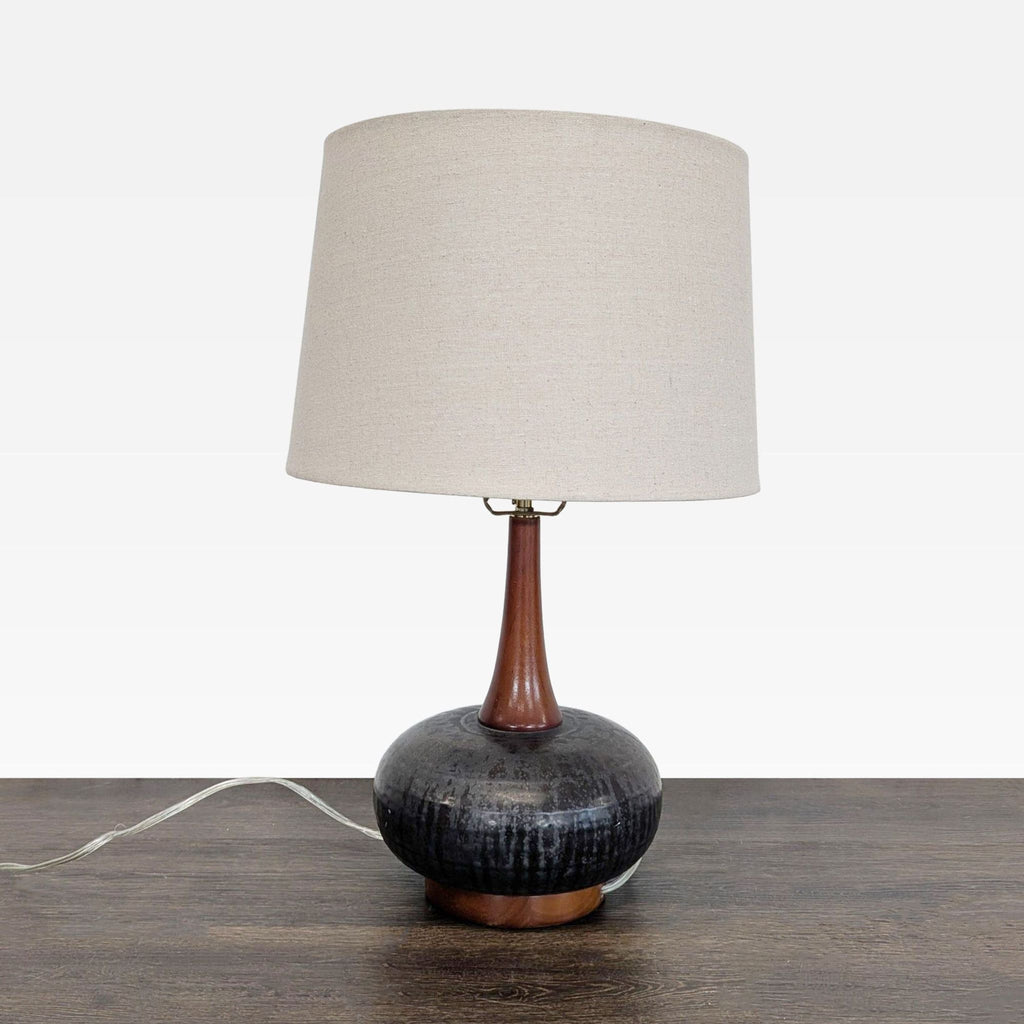 Mid-century modern table lamp with black ceramic base, wood accents, and beige fabric shade by 360 Lighting.
