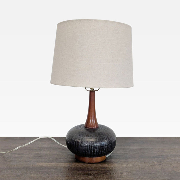 Mid-century modern table lamp with black ceramic base, wood accents, and beige fabric shade by 360 Lighting.
