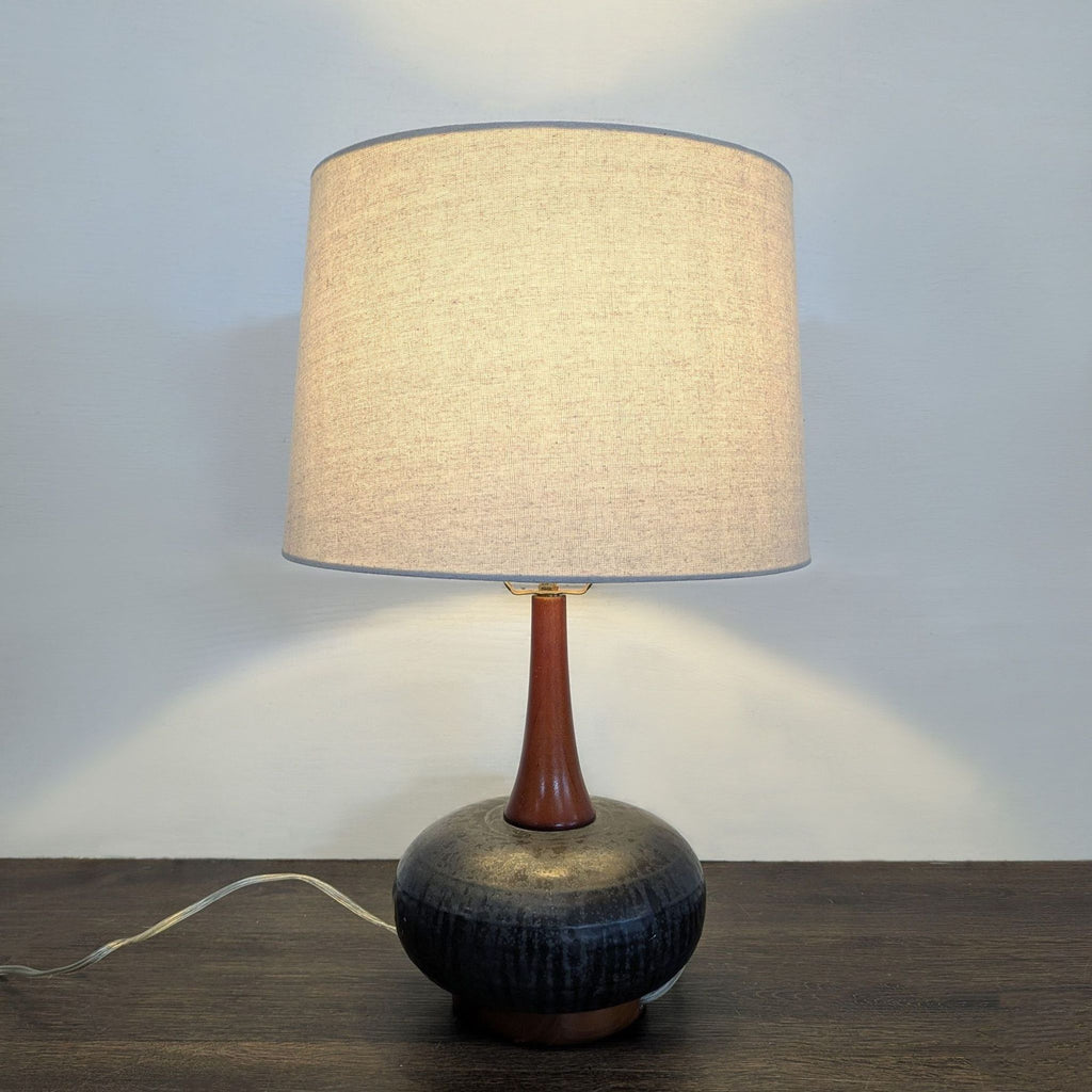Stylish black ceramic lamp with warm wood touches and beige shade, ideal for living rooms or bedrooms.