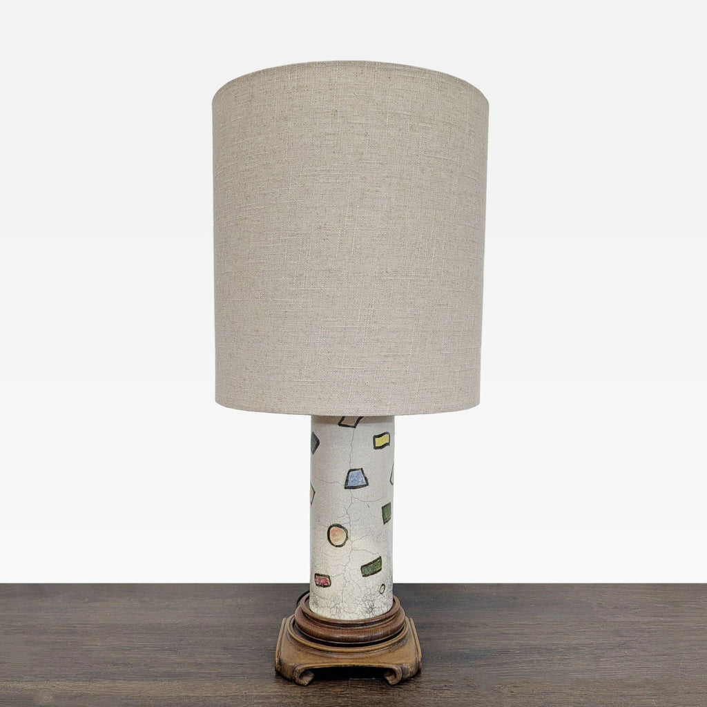 Tall table lamp with colorful geometric ceramic base, fabric drum shade, and wooden stand for stylish lighting.  
