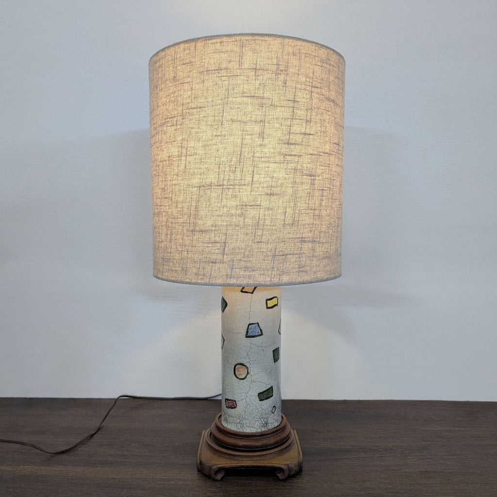 Modern table lamp featuring a patterned ceramic base, neutral drum shade, and classic wood stand for cozy spaces.  