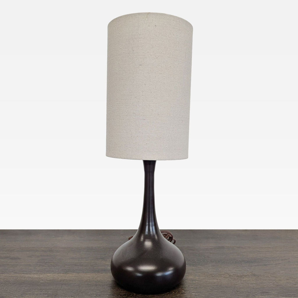 Modern table lamp with a curvy black base and tall beige cylinder shade, ideal for stylish indoor lighting.