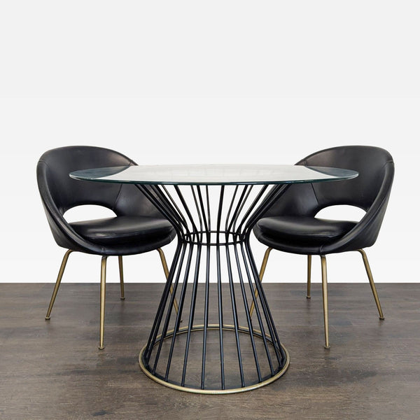 Pottery Barn dining set with round glass table, black metal wire base, and two black chairs with brass legs.