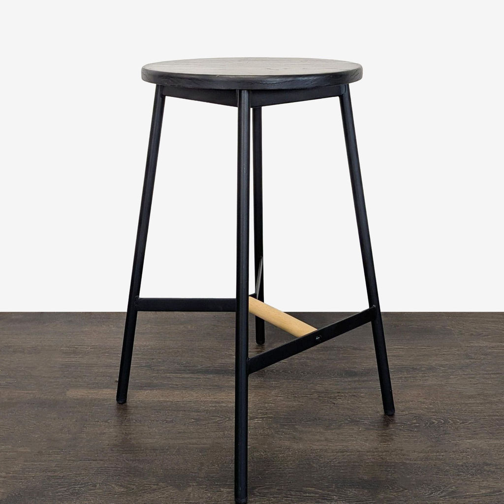 Minimalist black stool featuring a circular seat, wood accent footrest, and sturdy metal frame for versatile use.