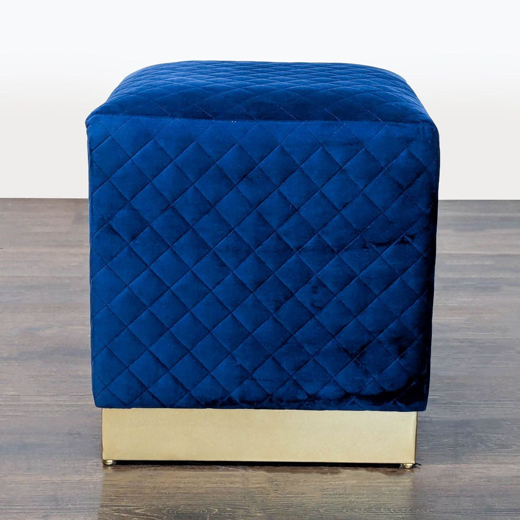 Blue velvet cube ottoman with quilted pattern and gold base, perfect as a stool or footrest.