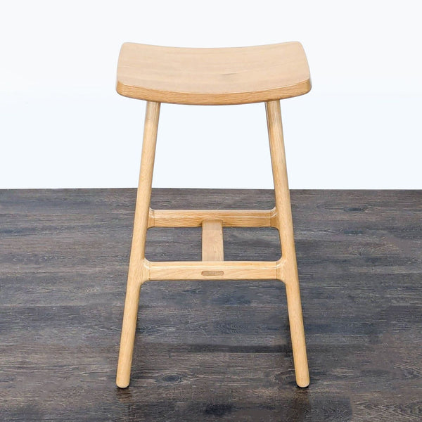 Modern solid wood stool by Article featuring a curved seat and minimalist Scandinavian design, ideal for bar spaces.