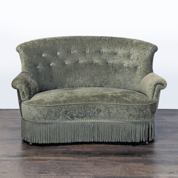 Vintage green velvet loveseat with tufted back, rolled arms, and fringe skirt in classic style.