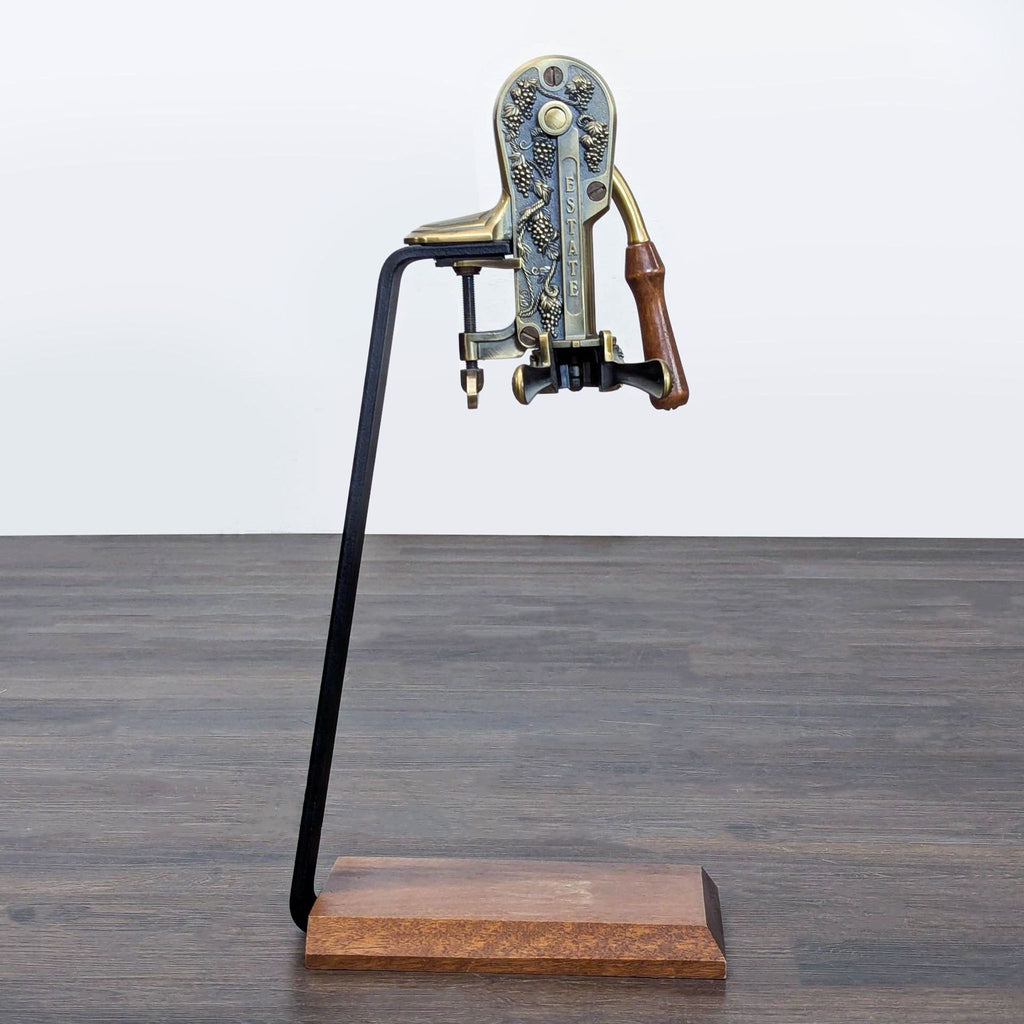 Antique-style Rogar Estate wine opener with grapevine details, brass-tone finish, and wood handle on display stand.  