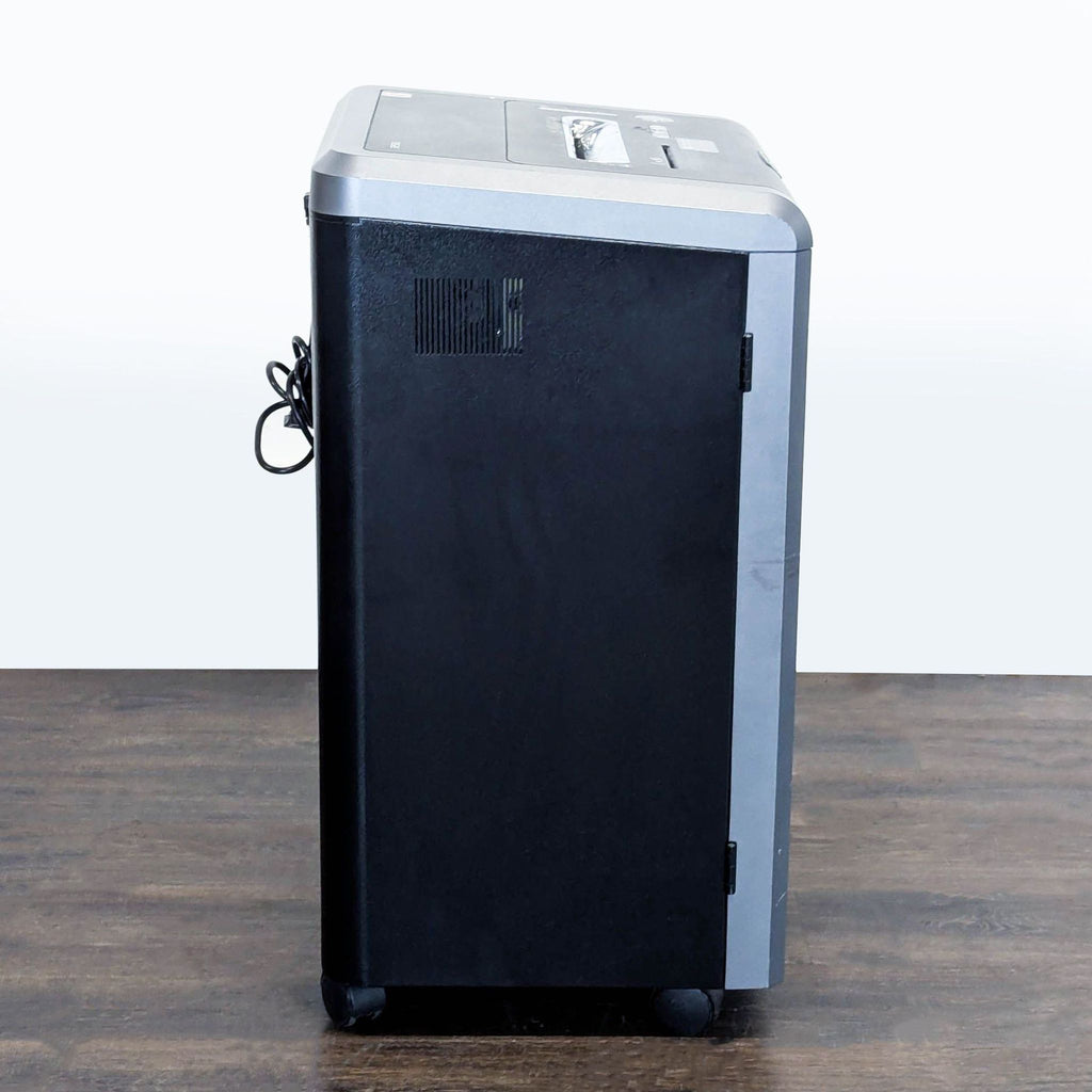 2. Side view of a Fellowes black and silver shredder with power cord, placed on a wooden floor.
