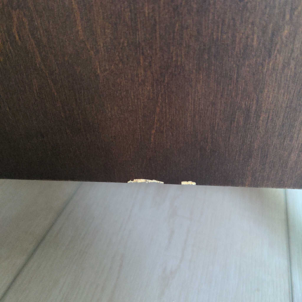3. Zoomed-in image of a wood dresser's bottom edge displaying a small chipped area on the finish.