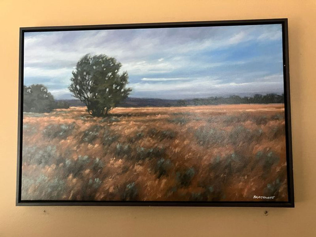 1. Framed painting of a tree in a golden field under a blue sky with clouds, hanging on a beige wall.