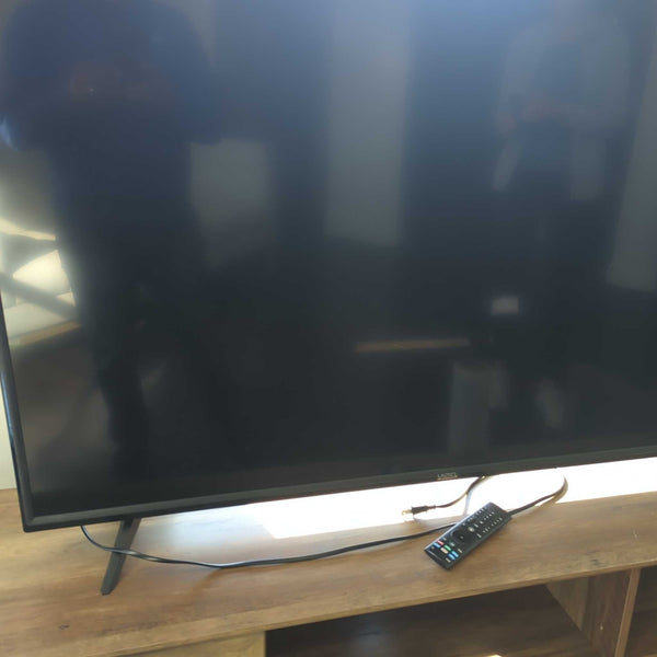 1. Vizio TV standing on a wooden table, powered off, with a remote and power cable in front of the screen.