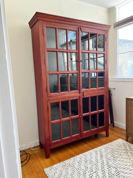 1. Crate & Barrel hutch with glass panel doors, reddish wood frame, and interior shelving, in a sunlit room.