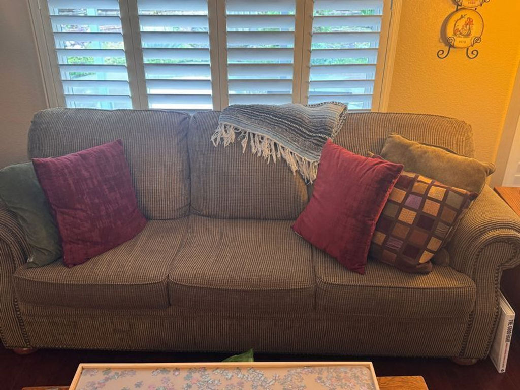 1. Brown Reperch 3-seat sofa with red and patterned pillows, placed in a cozy living room by window shutters.
