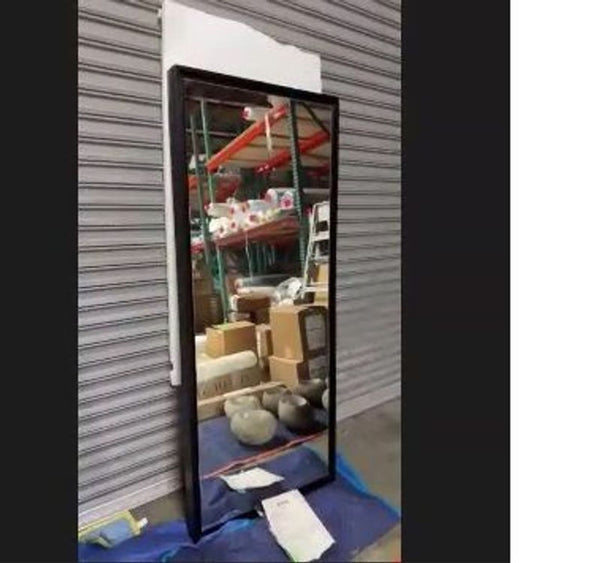 1. Tall rectangular West Elm wall mirror with black frame, reflecting storage items in a warehouse setting.