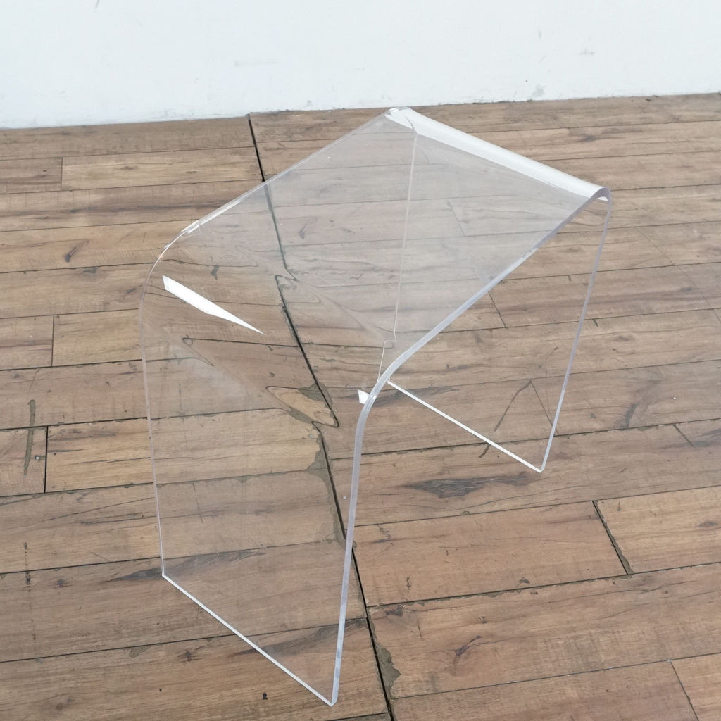 2. Side view of a clear acrylic Reperch end table in waterfall style on a wooden floor background.