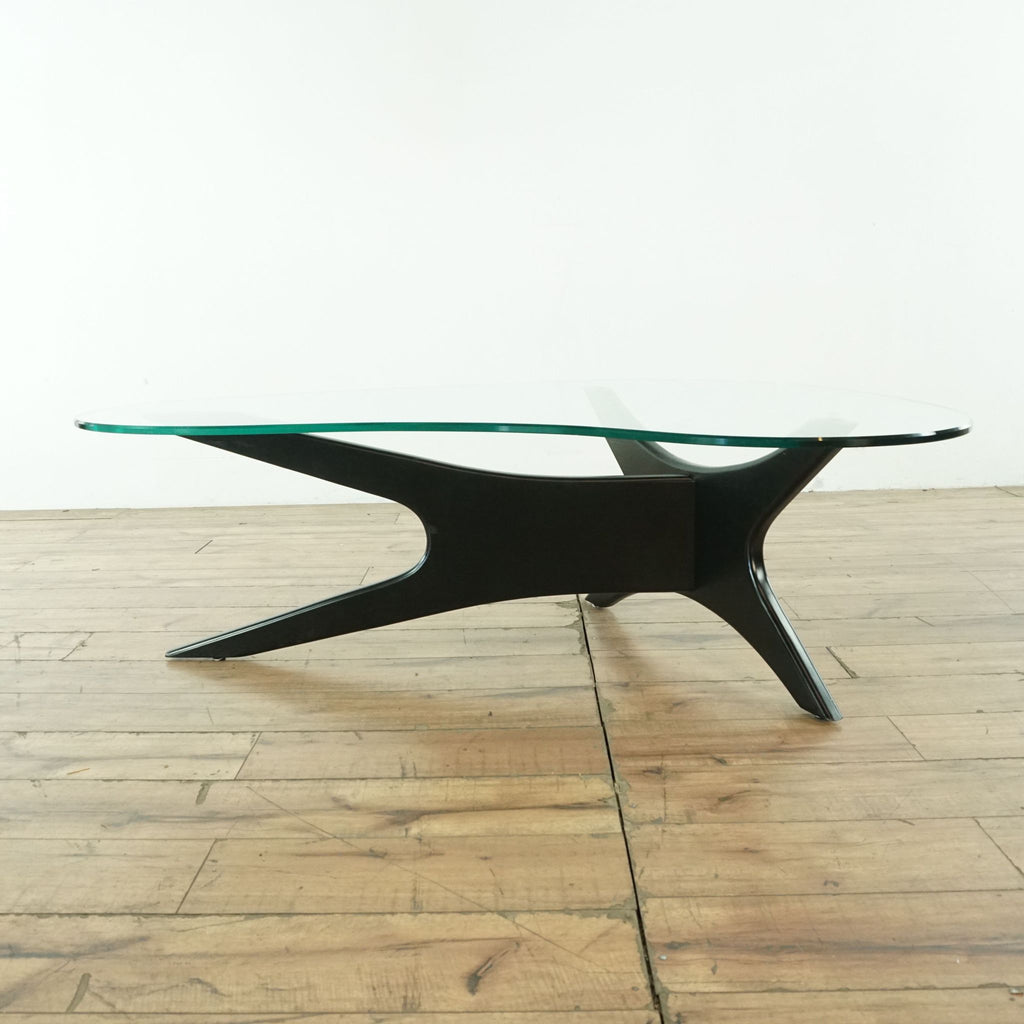 3. Side profile of Scandinavian Designs coffee table with clear kidney-shaped glass top and sleek abstract wooden base.