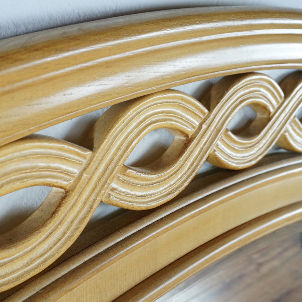 2. Close-up of light wood mirror frame showing carved, intertwined pattern along the arched top edge.
