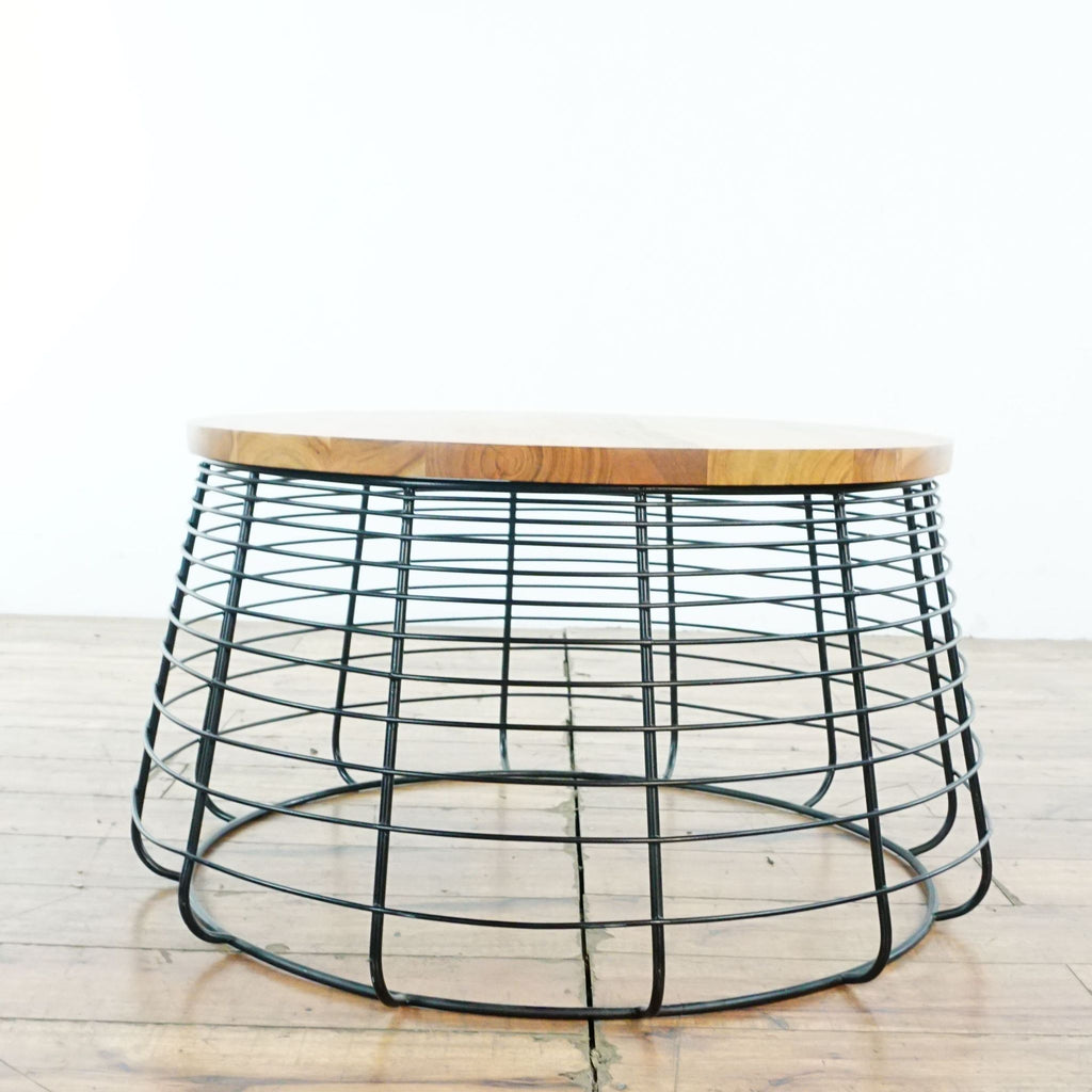 Round coffee table by CB2 featuring a black wire base and smooth wood top on a wooden floor.