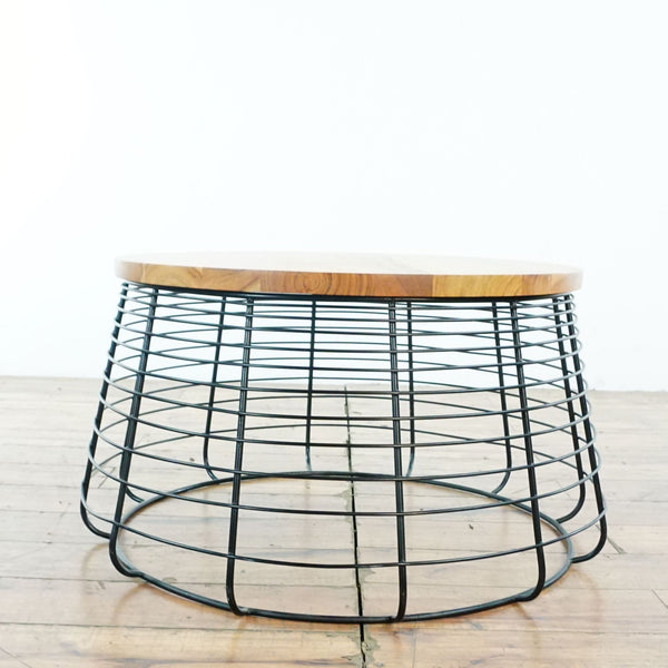 Round coffee table by CB2 featuring a black wire base and smooth wood top on a wooden floor.