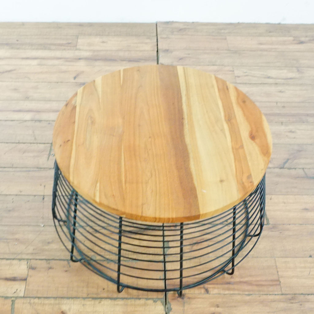 Top view of a CB2 coffee table with circular wood surface and black wire frame base.