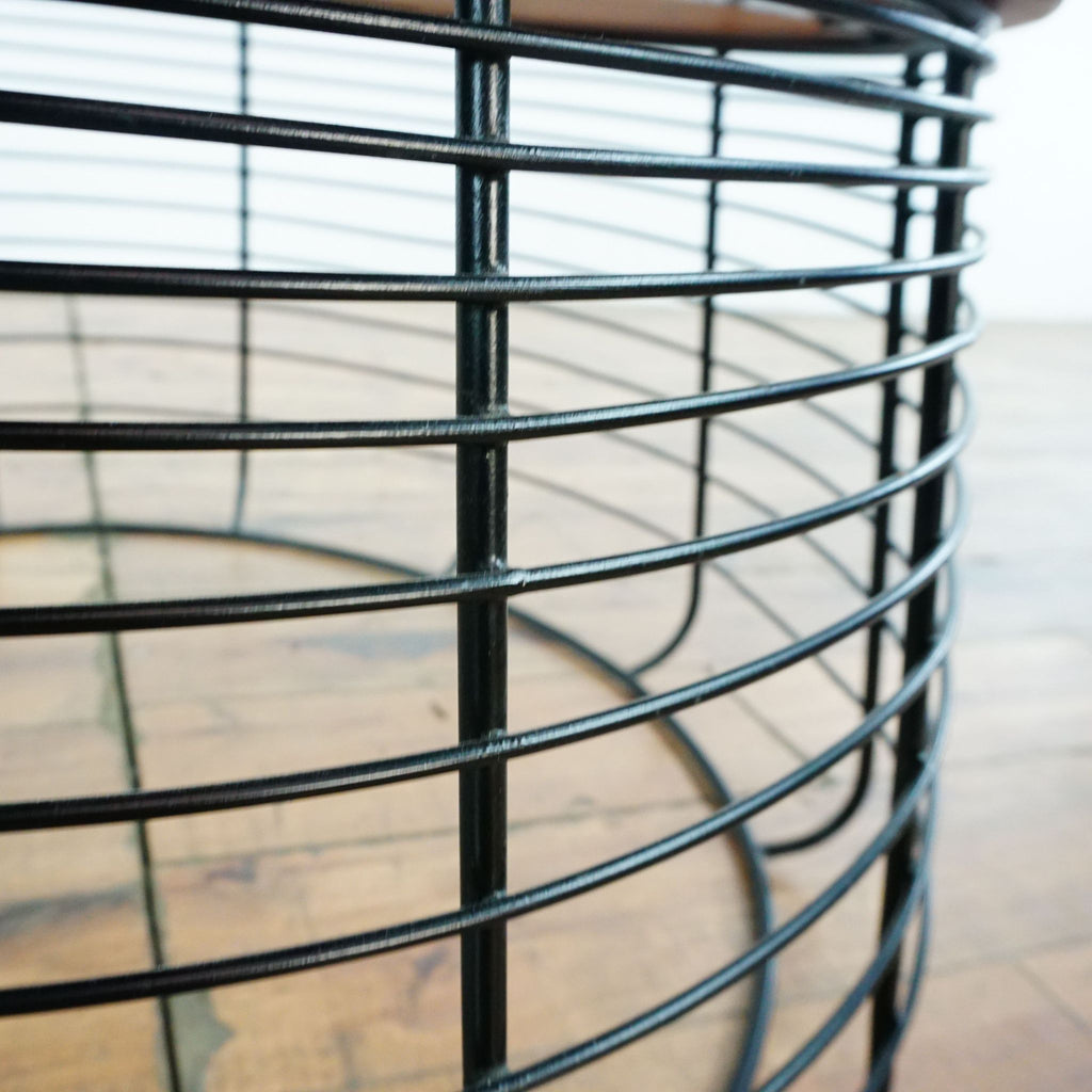 Close-up of the CB2 coffee table's black wire base, showing metal detailing and wood tabletop above.