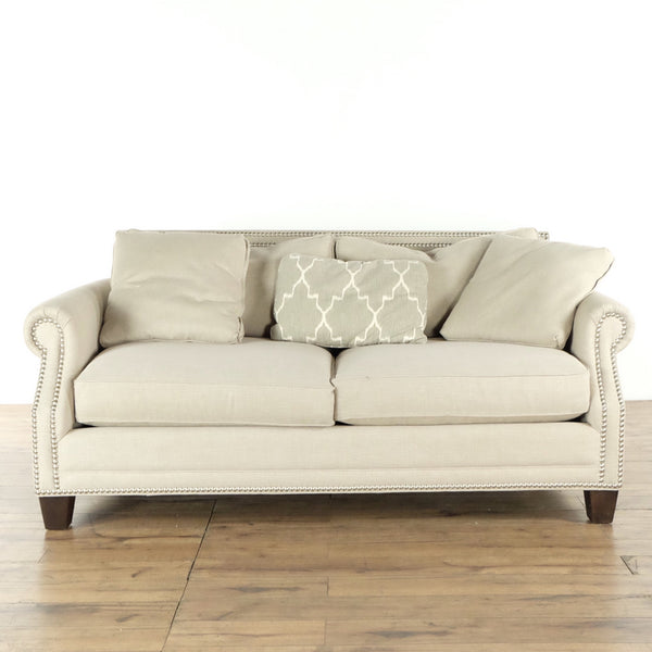 Front view of an H.D. Buttercup sofa with nailhead trim, rolled arms, throw pillows, and wood feet.  