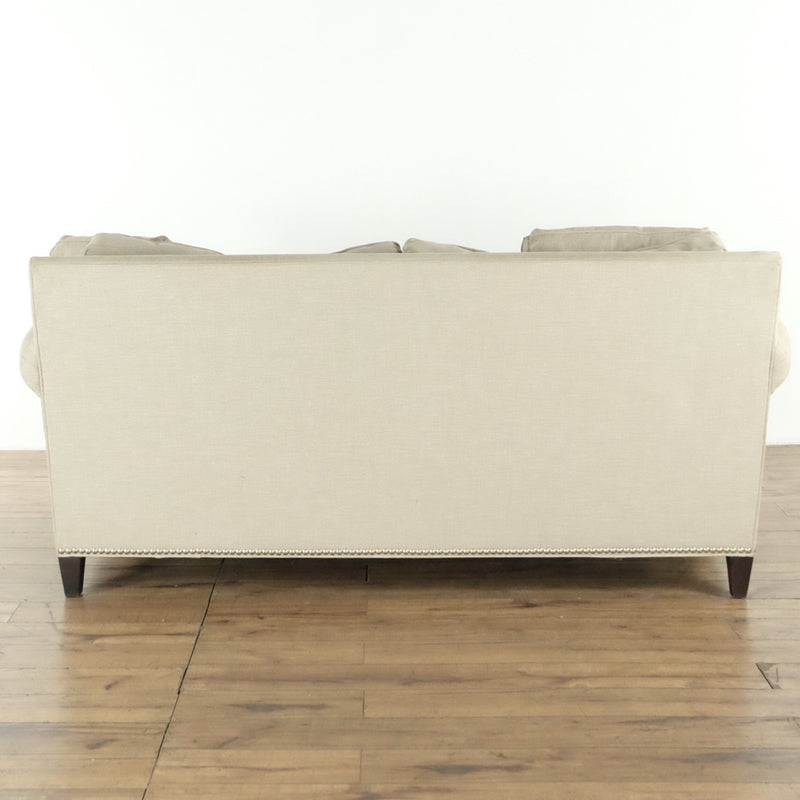 Rear view of a beige H.D. Buttercup sofa featuring simple lines and a nailhead trim along the bottom edge.