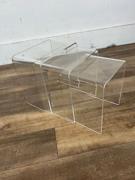 Clear acrylic nesting tables on a wooden floor, designed by West Elm.