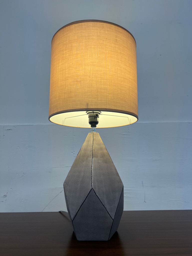 3. Neutral-colored Reperch lamp lit up, featuring a faceted base and a simple cylindrical fabric shade.