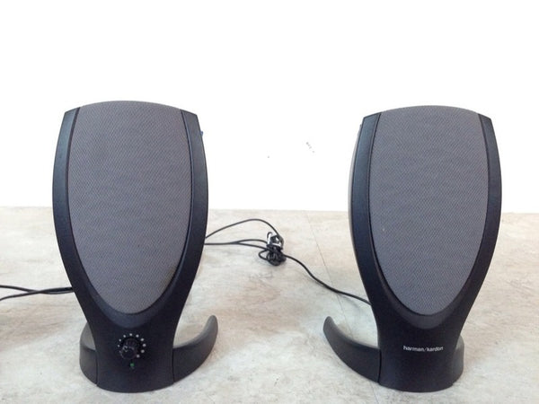 1. Pair of Harman/Kardon speakers with cords included, featuring a sleek, curved design, on a light surface.