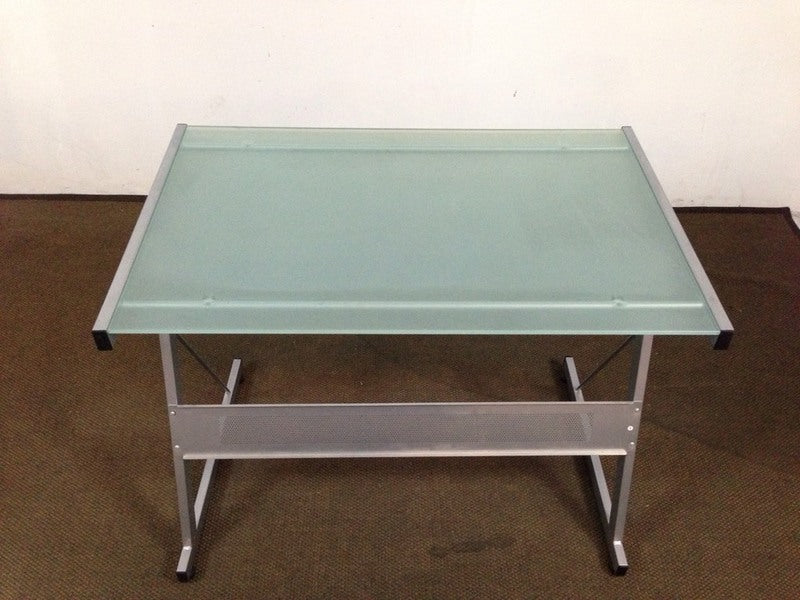 1. Reperch desk with slanted metal legs and a frosted glass top, viewed from the front on a brown carpet.