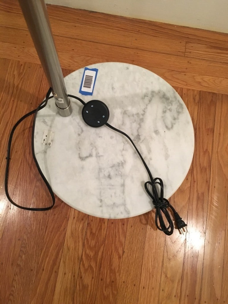 2. Close-up of the Reperch floor lamp’s round marble base with power cord and chrome pole, on wood floor.