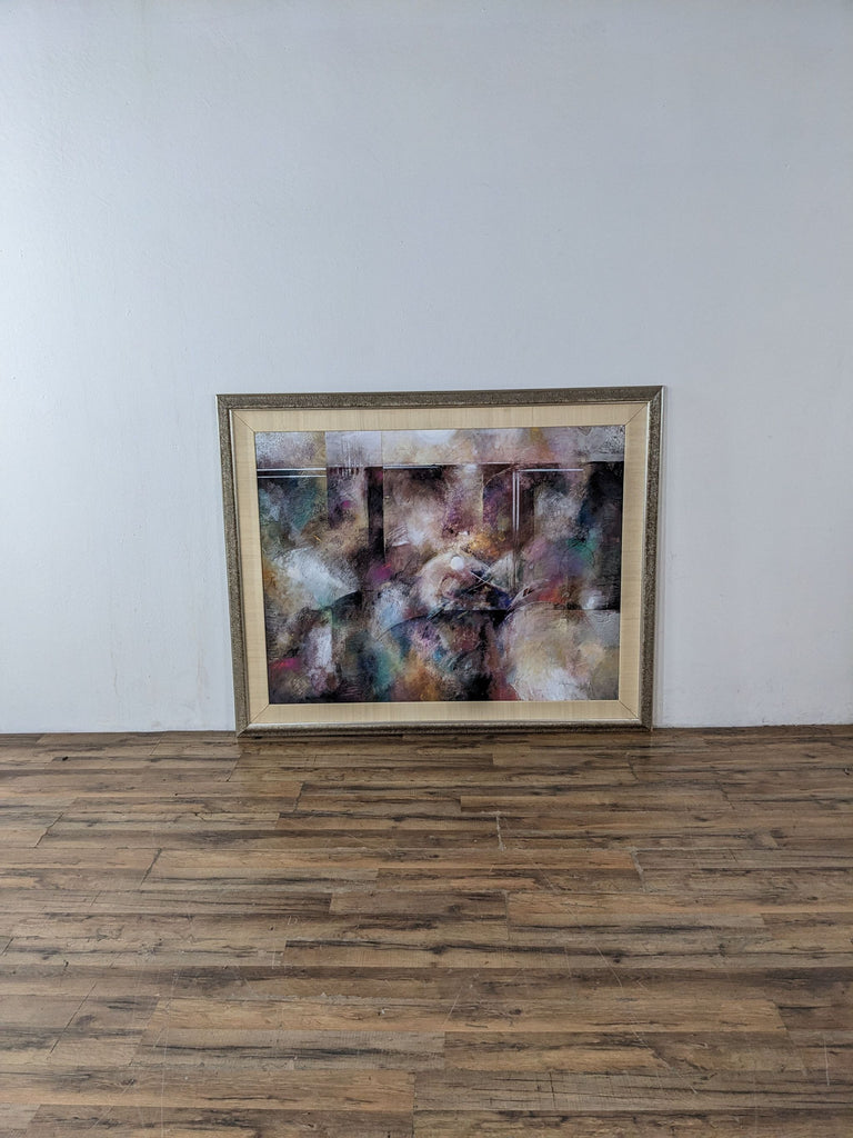 Framed abstract painting with colorful brush strokes displayed against a plain wall.