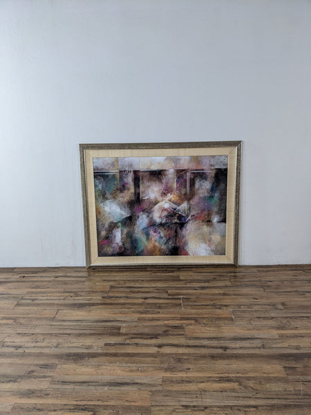 Framed abstract painting with colorful brush strokes displayed against a plain wall.