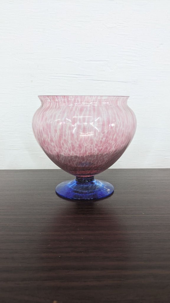 Ornate pink glass vase with a blue stand, by Reperch, against a white background on a dark tabletop.