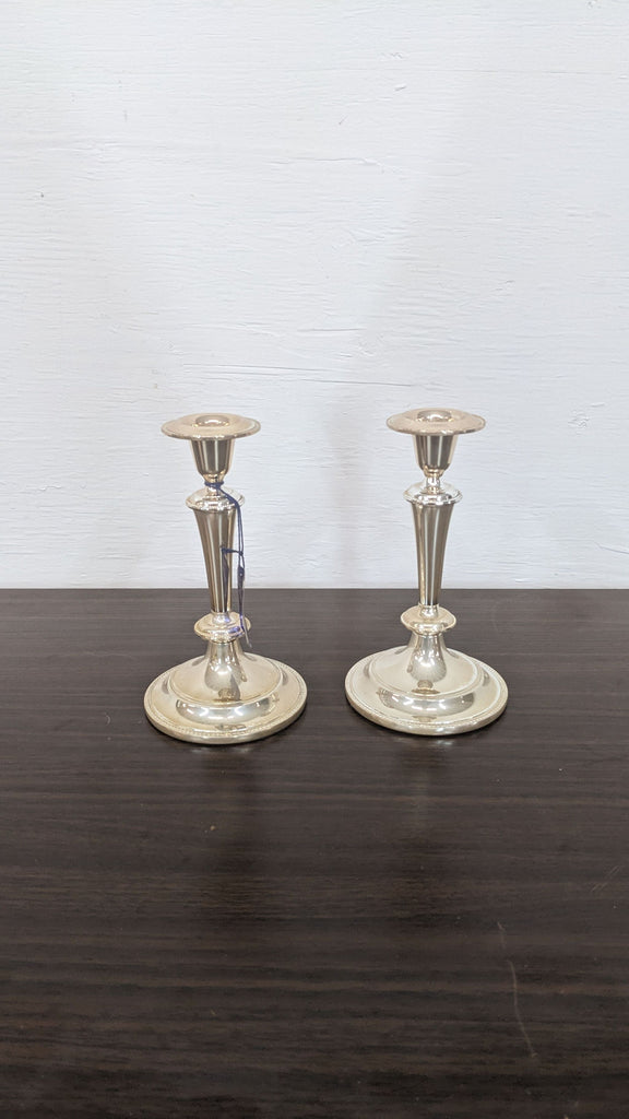 Two silver candlesticks with tapered design on a dark surface.