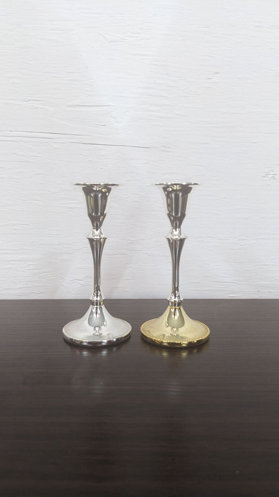 Two elegant Reperch candle holders, silver and gold, on a dark surface.