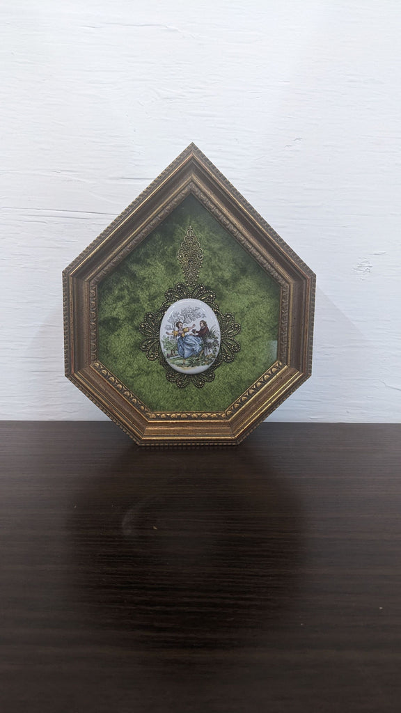 Antique-style frame displaying a classic painted scene on velvet, bordered with intricate detailing.