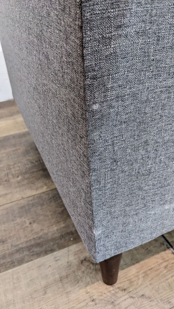 Close-up of gray sofa fabric and textured texture, showing tapered wood feet.
